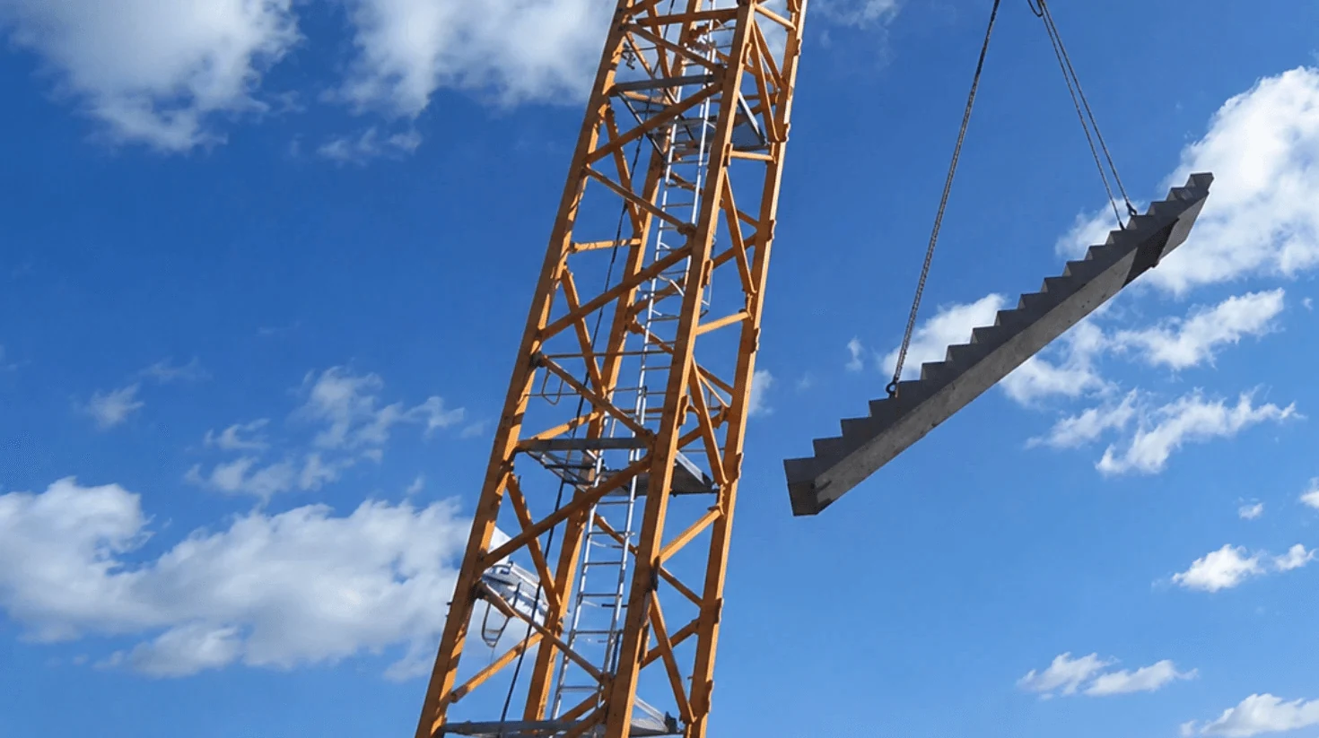 Precast concrete stair section being hoisted on a construction site.